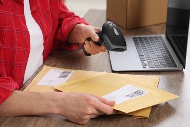 Photo of Seller with scanner reading parcel barcode at table in office, closeup. Online store