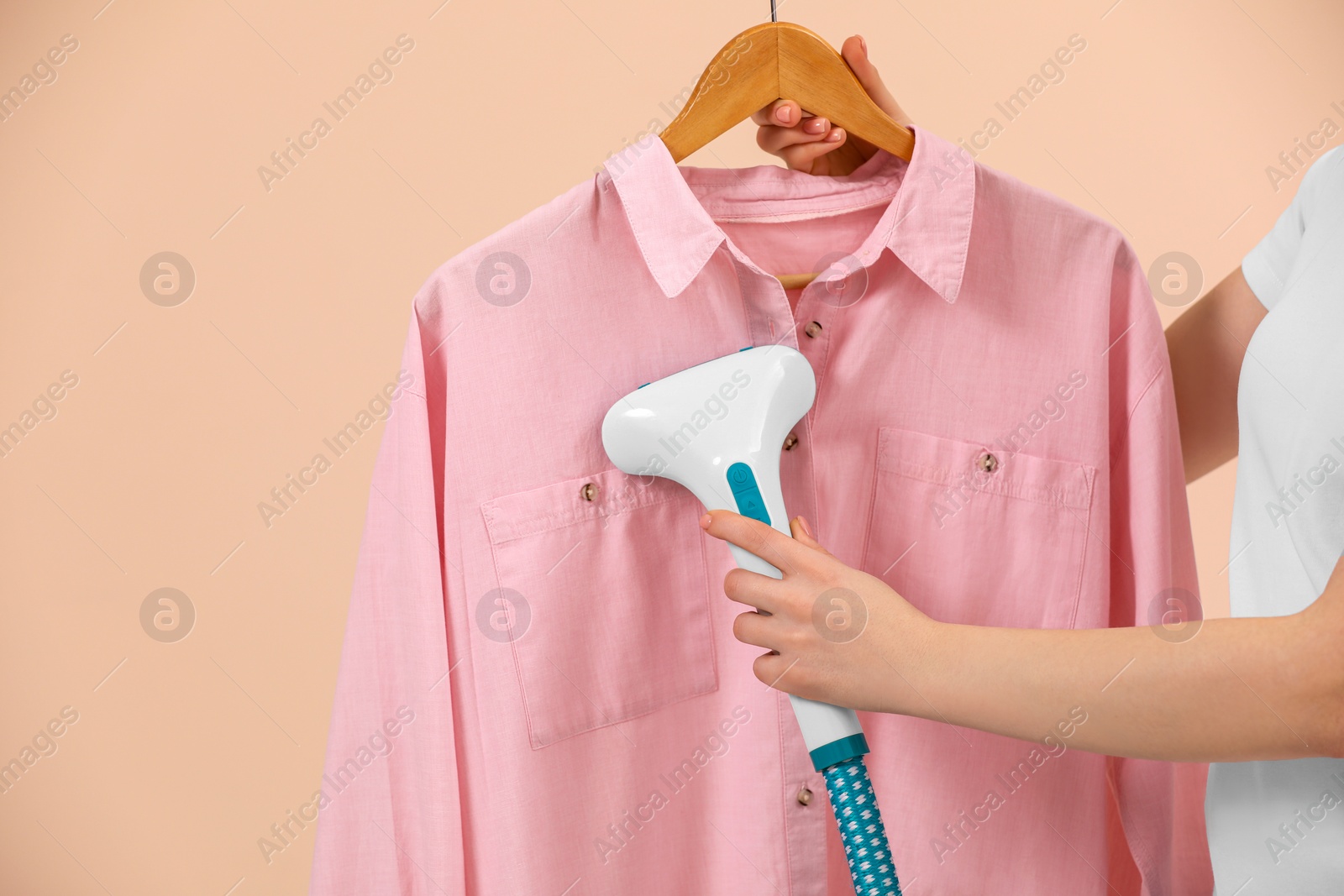 Photo of Woman steaming shirt on hanger against beige background, closeup