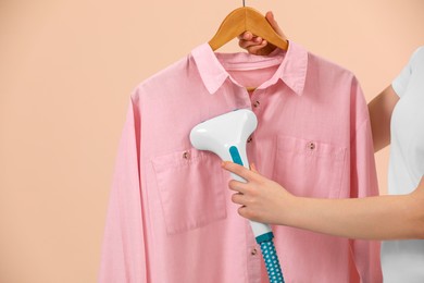 Woman steaming shirt on hanger against beige background, closeup