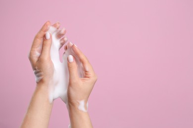 Photo of Skin care cosmetic. Woman washing hands with cleansing foam on pink background, closeup and space for text