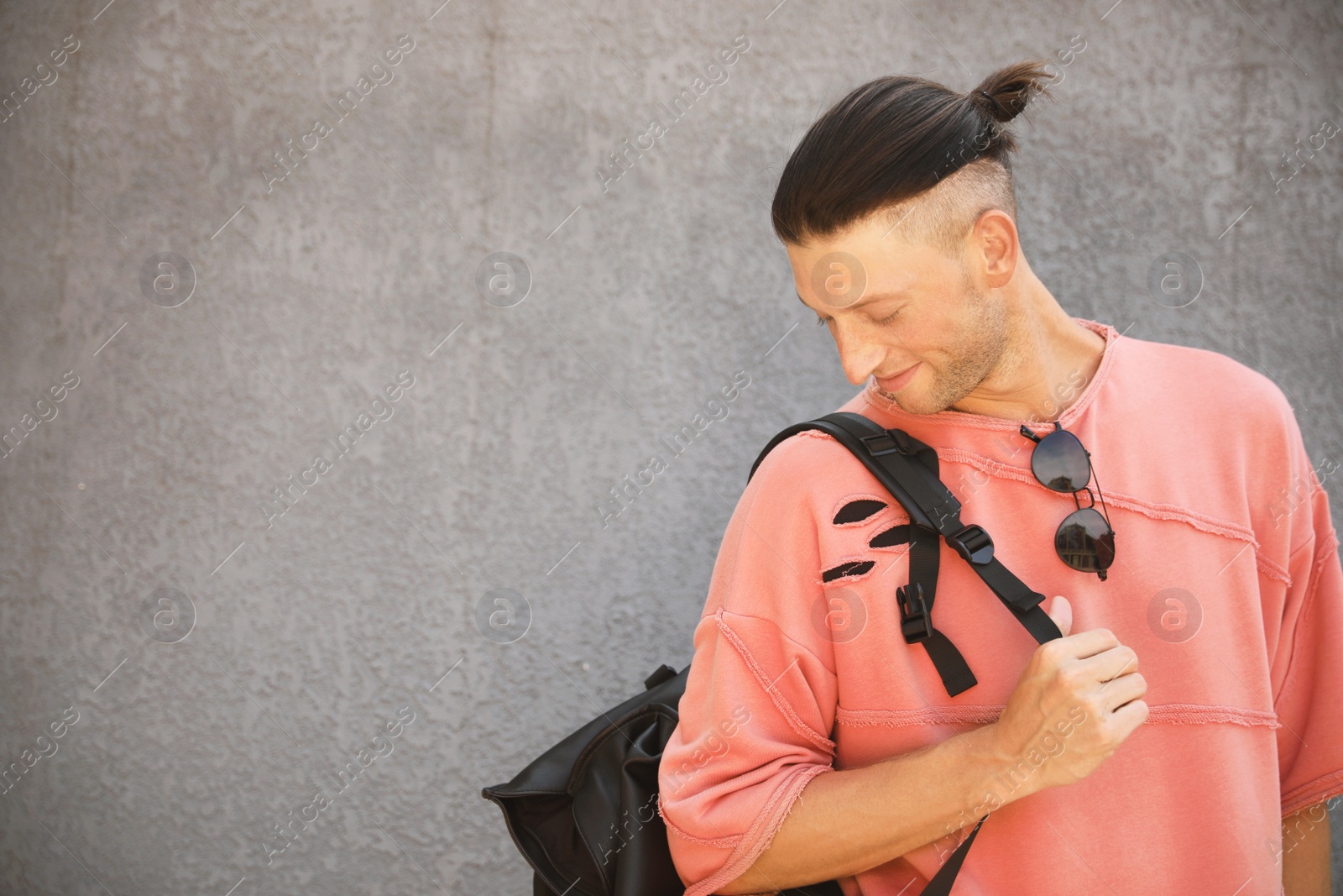 Photo of Handsome young man with stylish sunglasses and backpack near grey wall, space for text