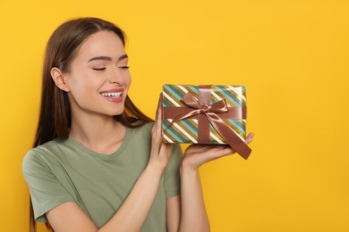 Photo of Happy young woman with gift box on yellow background