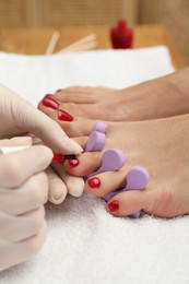 Photo of Pedicurist painting client`s toenails with red polish in beauty salon, closeup