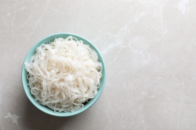 Photo of Bowl of tasty cooked rice noodles on light grey table, top view. Space for text