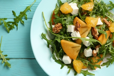 Delicious persimmon salad with arugula and walnuts on light blue wooden table, closeup