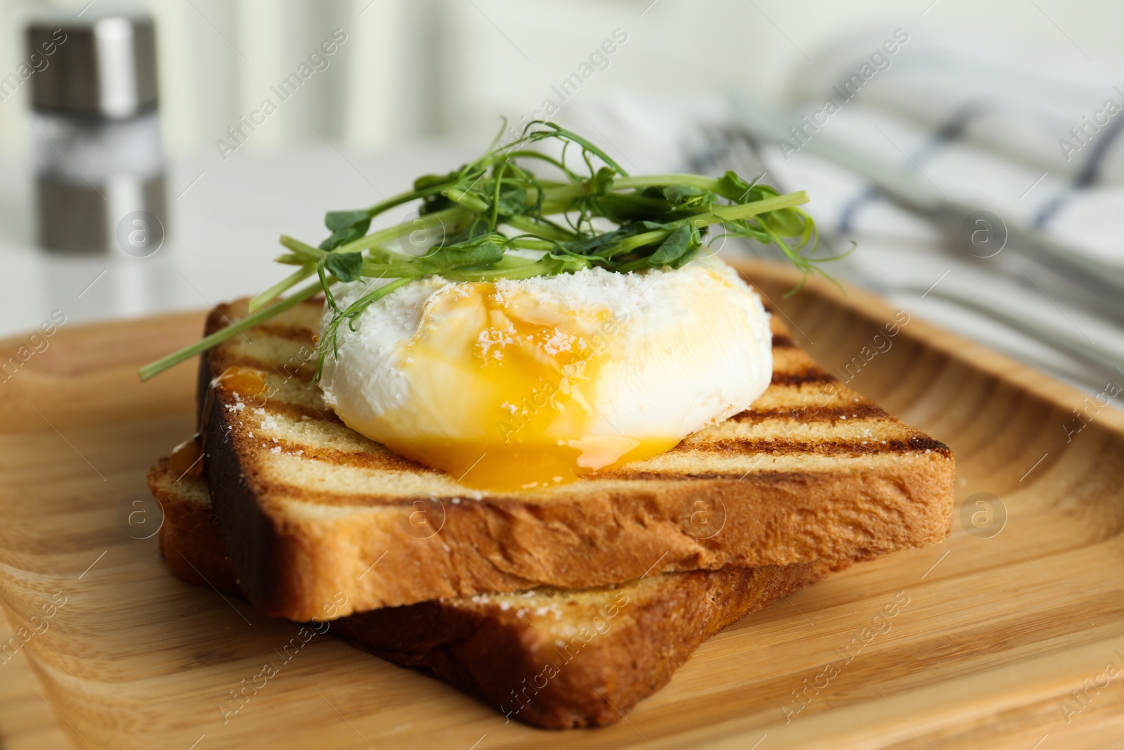 Photo of Delicious poached egg with toasted bread and sprouts served on wooden plate, closeup