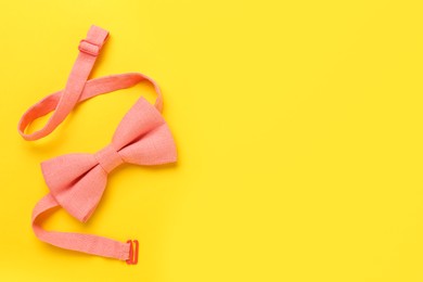 Photo of Stylish pink bow tie on yellow background, top view. Space for text