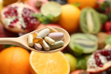 Photo of Different vitamin pills in spoon over fresh fruits, closeup. Space for text