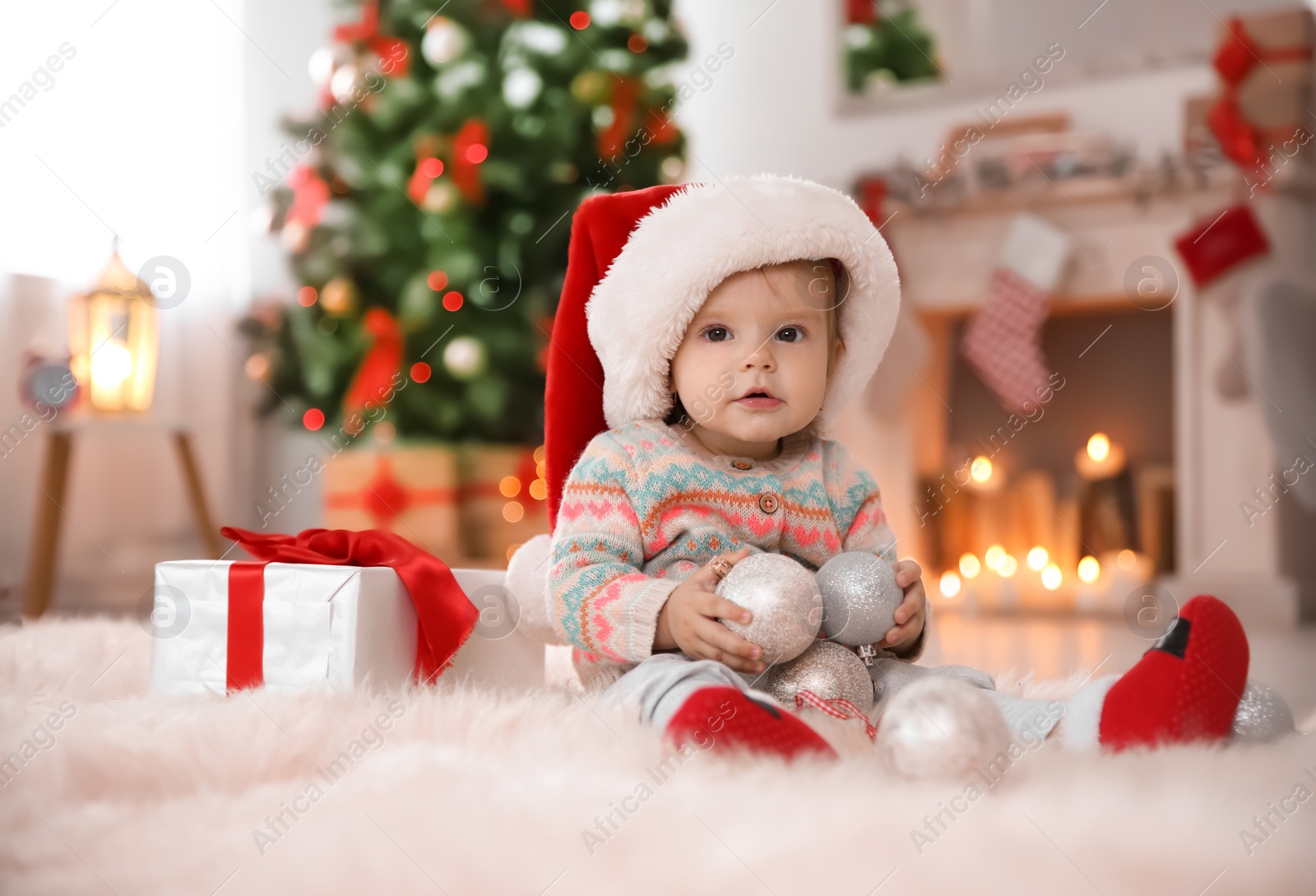 Photo of Cute little baby in Santa hat sitting on fur rug at home. Christmas celebration