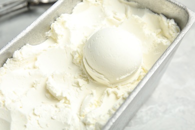 Photo of Container with delicious vanilla ice cream on table, closeup