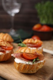 Delicious profiteroles with cream cheese, jamon and tomato on wooden board, closeup