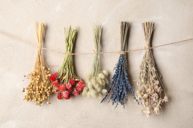 Photo of Bunches of beautiful dried flowers hanging on rope near light grey wall