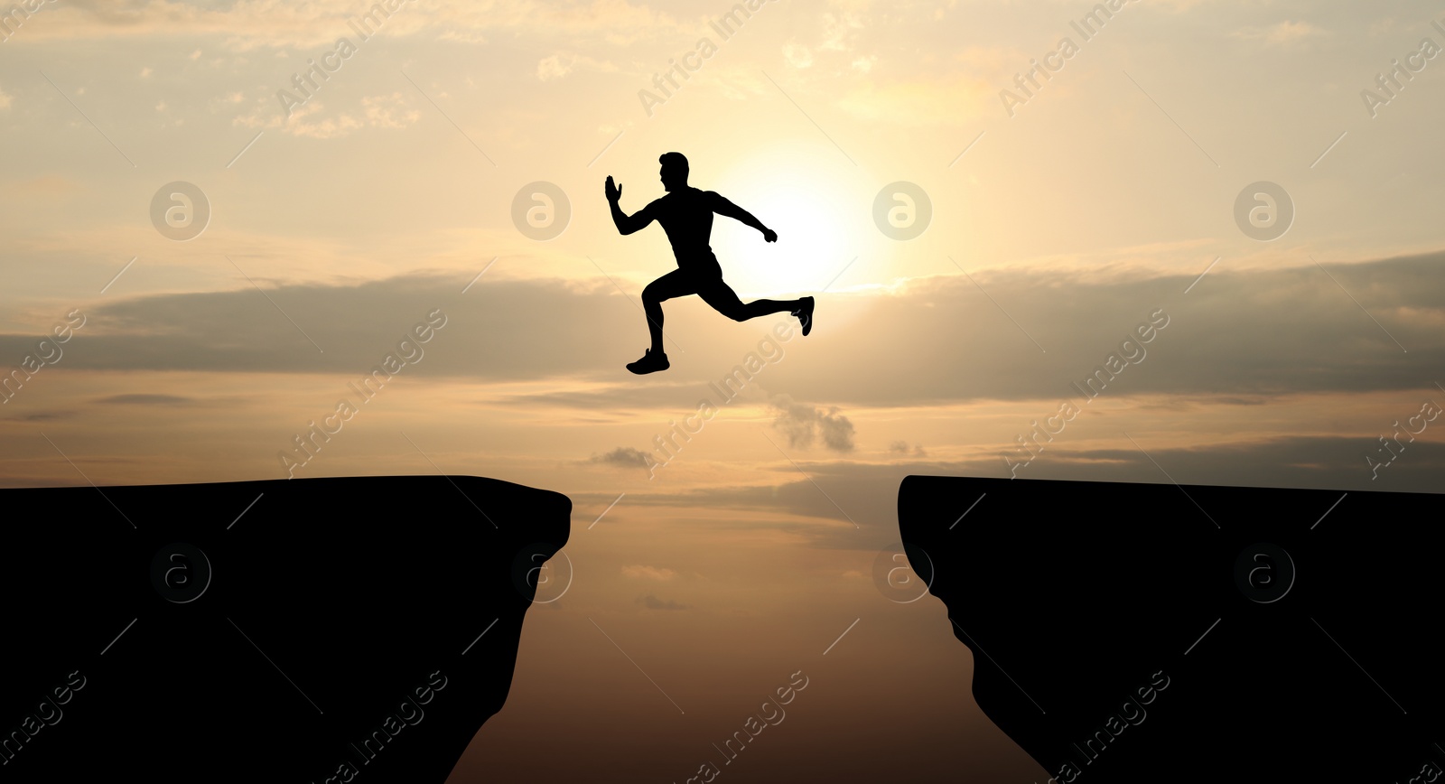 Image of Concept of reaching life and business goals. Silhouette of man jumping over chasm at sunrise