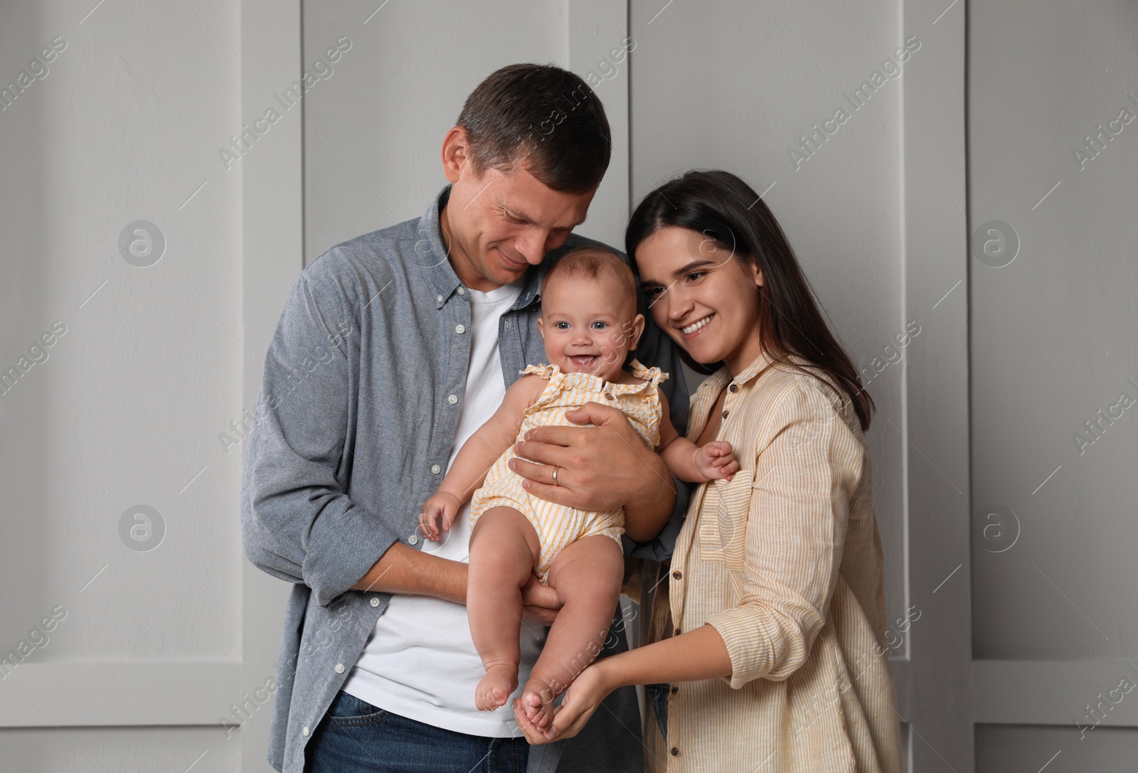 Photo of Happy family. Couple with their cute baby near light wall