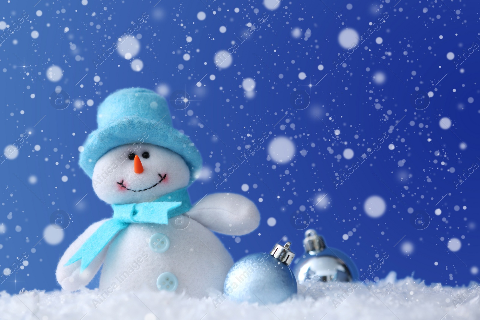 Image of Cute snowman and Christmas balls on snow against blue background, bokeh effect. Space for text 