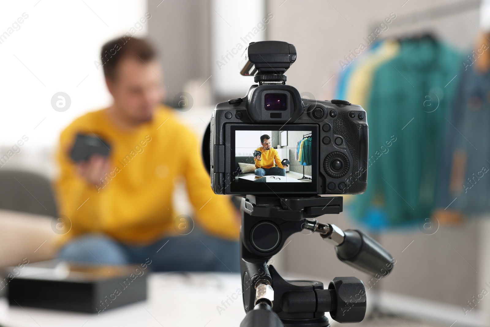 Photo of Fashion blogger showing wristwatches while recording video at home, focus on camera