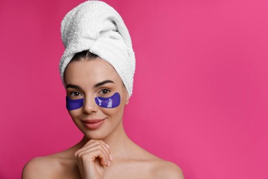 Beautiful young woman with under eye patches and hair wrapped in towel on pink background, space for text