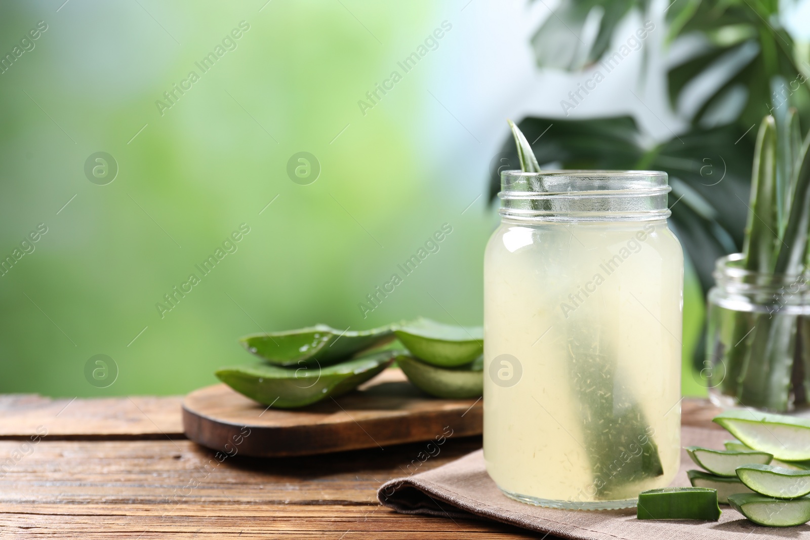 Photo of Fresh aloe juice in jar and cut leaves on wooden table outdoors. Space for text