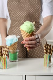 Photo of Woman holding waffle cone with cotton candy indoors, closeup