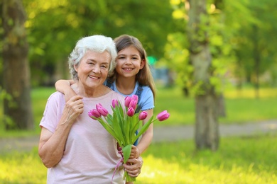 Photo of Little girl with her grandmother and bouquet of flowers in park. Space for text