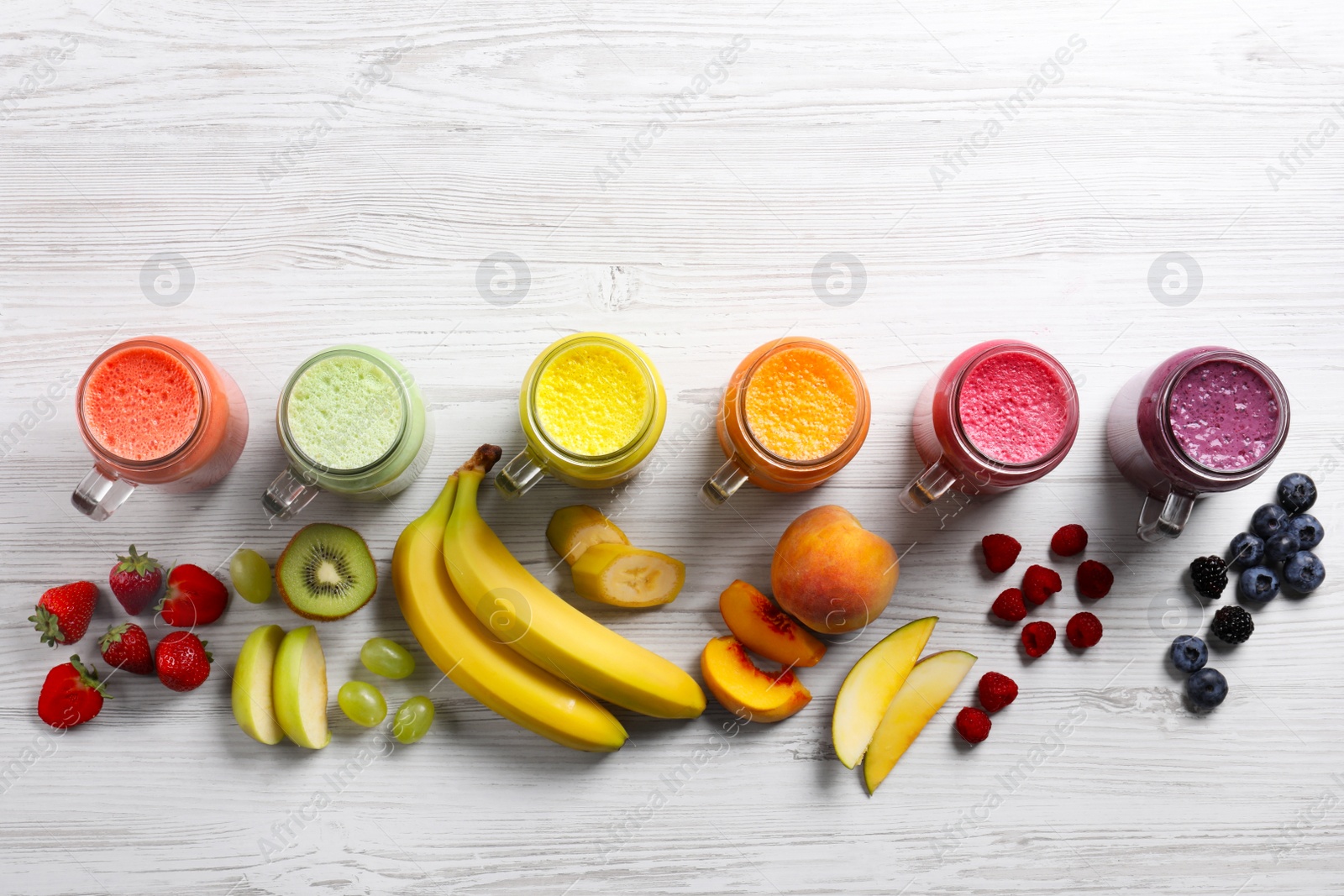 Photo of Many different tasty smoothies and ingredients on white wooden table, flat lay. Space for text