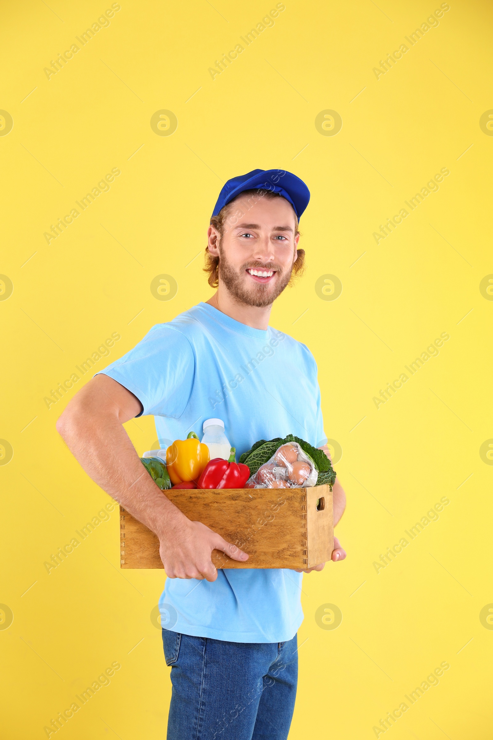 Photo of Delivery man holding wooden crate with food products on color background