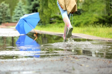 Woman in rubber boots running after umbrella on street, closeup. Rainy weather