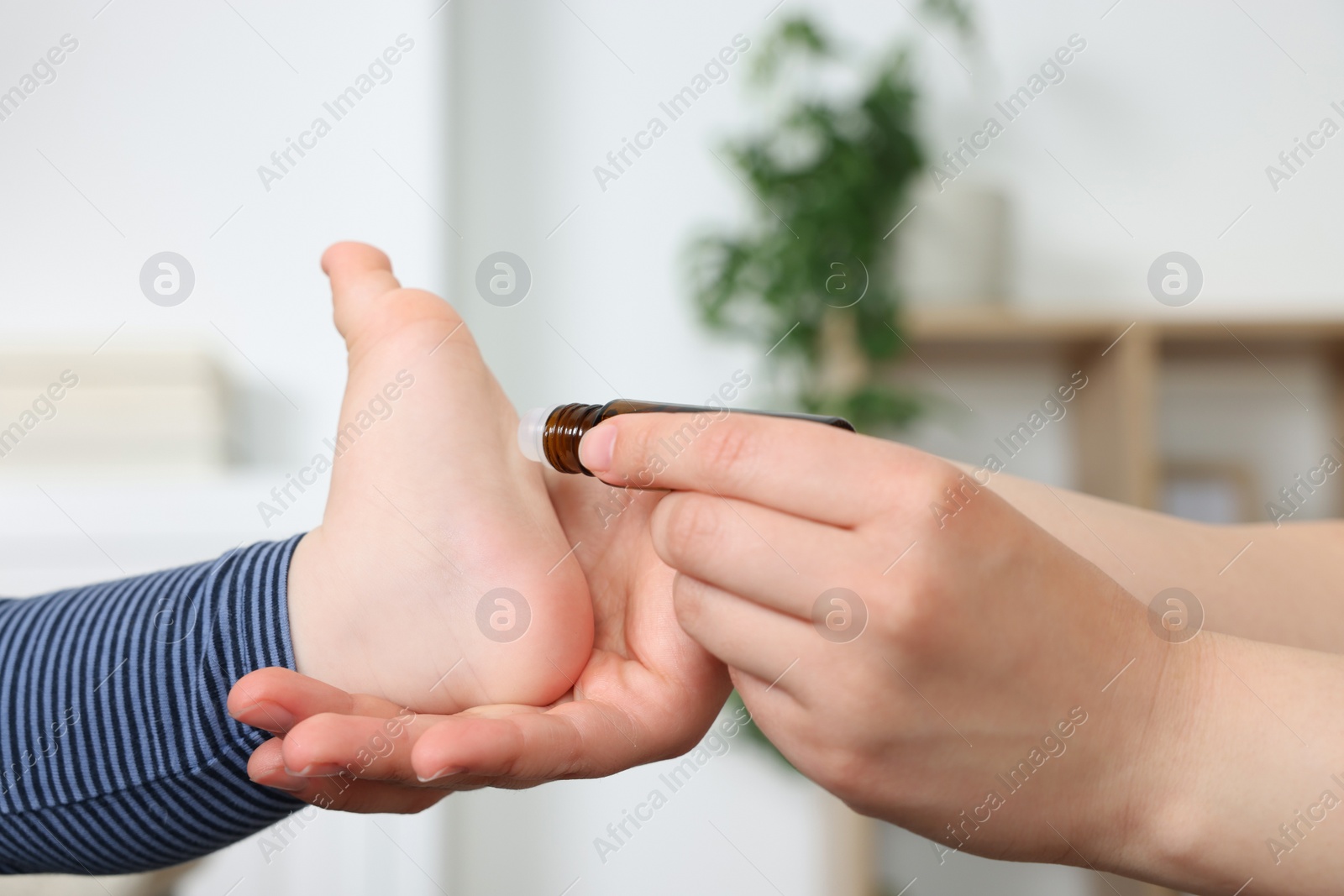 Photo of Mother applying essential oil from roller bottle onto her baby`s heel indoors, closeup