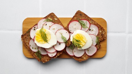 Photo of Tasty sandwiches with boiled egg and radish on white tiled table, top view