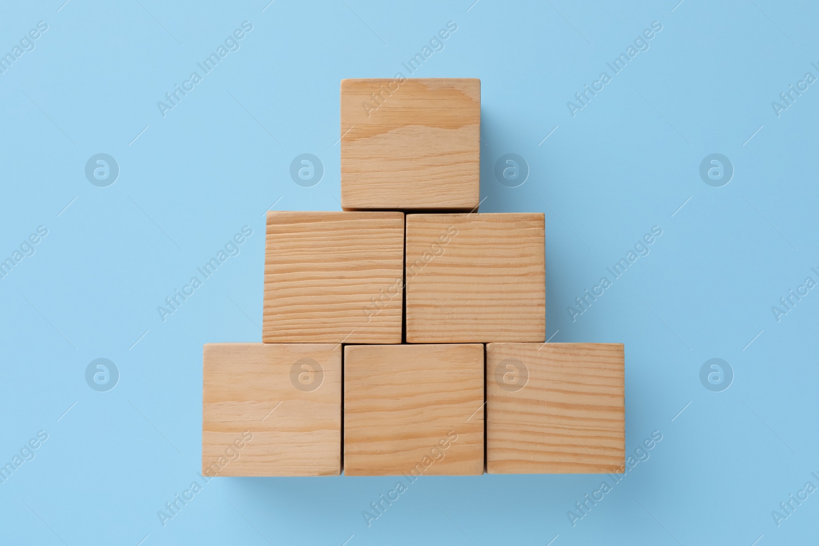 Photo of Pyramid made of wooden cubes on light blue background, top view. Management concept