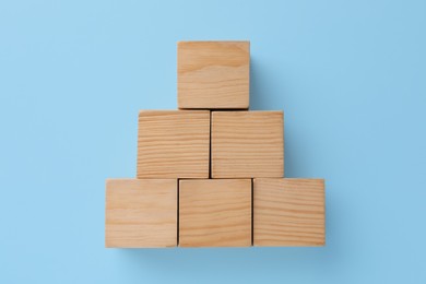 Pyramid made of wooden cubes on light blue background, top view. Management concept