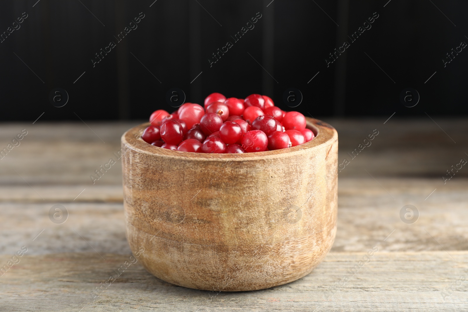 Photo of Ripe cranberries in bowl on wooden table