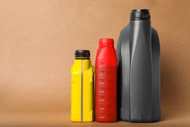 Photo of Motor oil in different canisters on light brown background, space for text