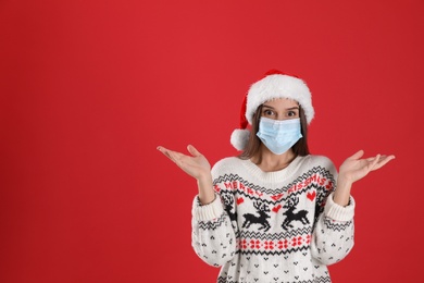 Emotional woman in Santa hat and medical mask on red background, space for text