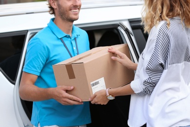 Photo of Young courier delivering parcel to woman outdoors