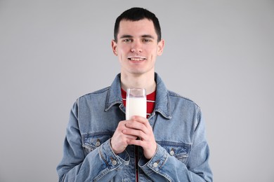 Happy man with milk mustache holding glass of tasty dairy drink on gray background