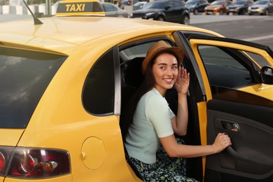 Photo of Beautiful young woman getting out of taxi on city street