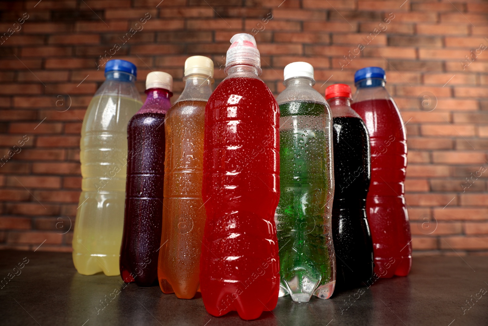 Photo of Bottles of soft drinks with water drops on table near brick wall