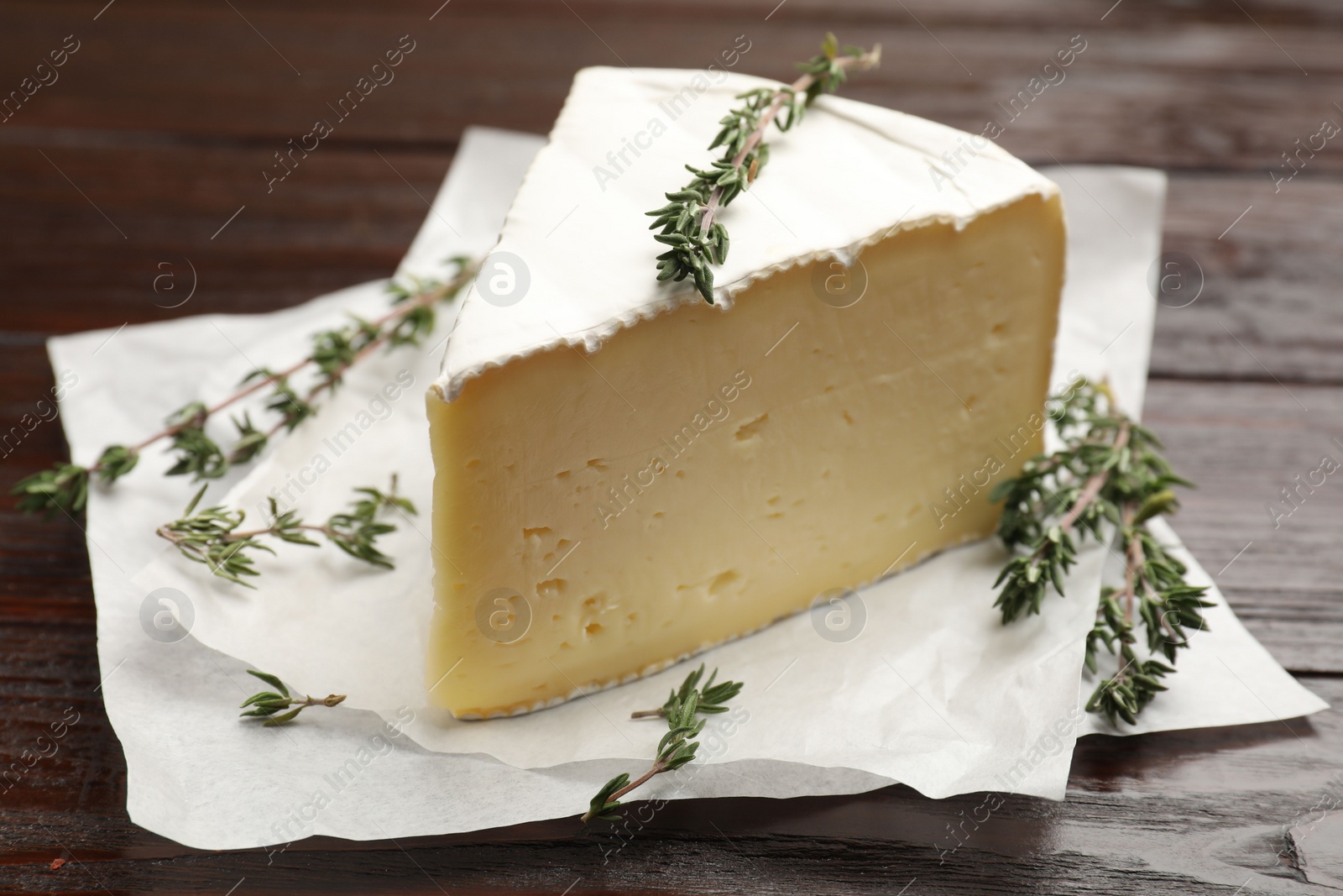 Photo of Piece of tasty camembert cheese and thyme on wooden table, closeup