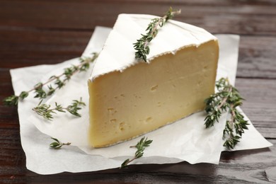 Photo of Piece of tasty camembert cheese and thyme on wooden table, closeup