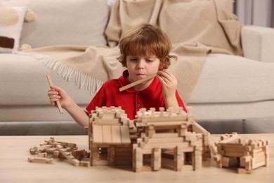 Cute little boy playing with wooden construction set at table in room. Child's toy