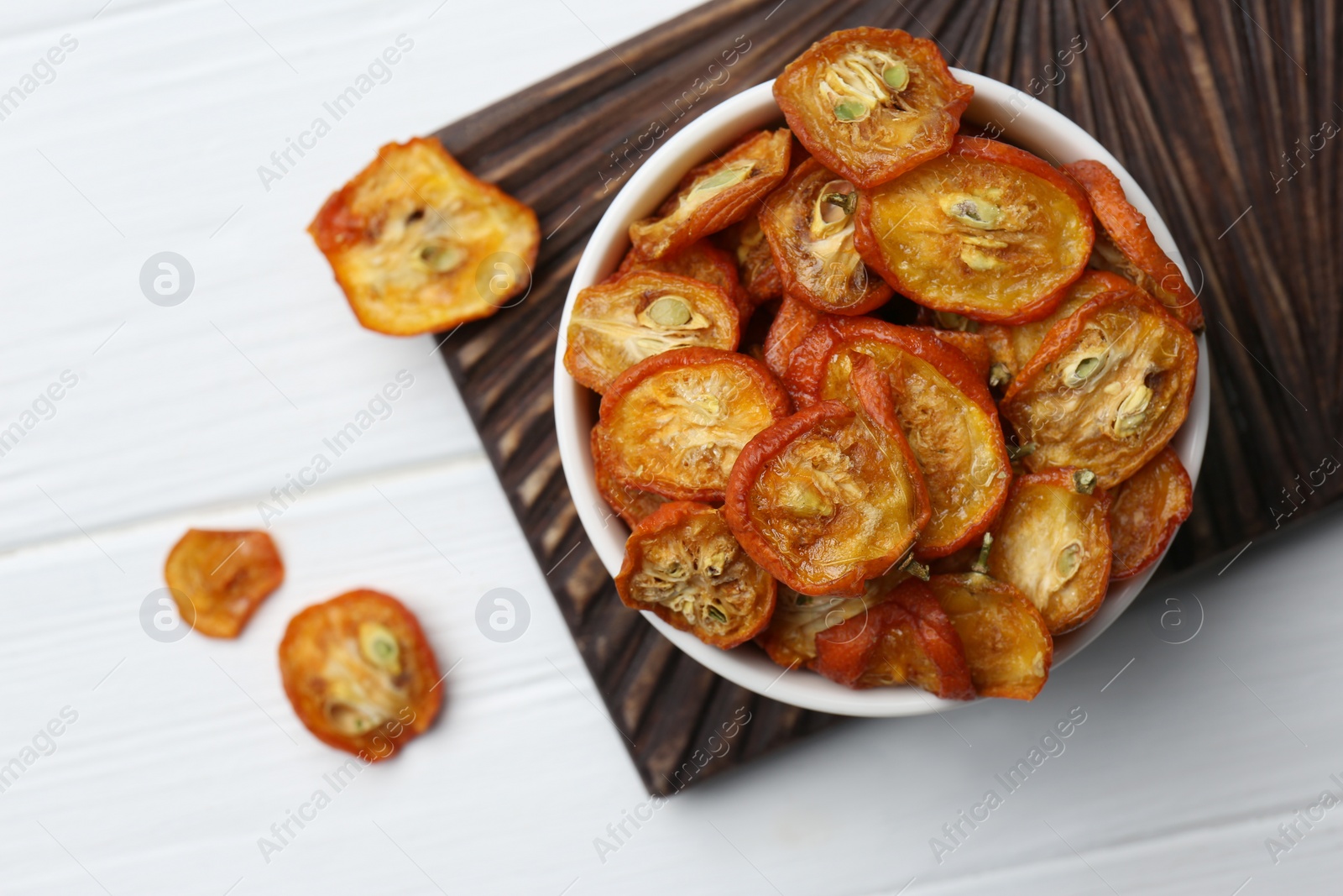 Photo of Bowl with cut dried kumquat fruits on white wooden table, flat lay