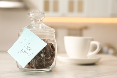 Photo of Glass jar full of cookies with romantic sticky note I Love You in kitchen