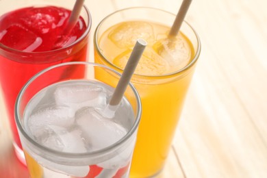 Photo of Glasses of different refreshing soda water with ice cubes and straws on table, closeup