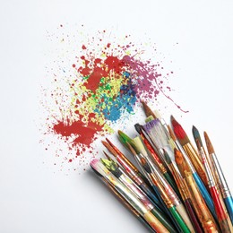 Different brushes and paint splatters on white background, top view