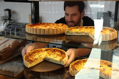 Photo of Happy seller taking tasty quiche from showcase in bakery shop