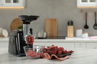 Photo of Electric meat grinder with beef mince on white table in kitchen, space for text