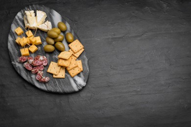 Photo of Toothpick appetizers. Pieces of cheese, sausage and olives on black table, top view with space for text