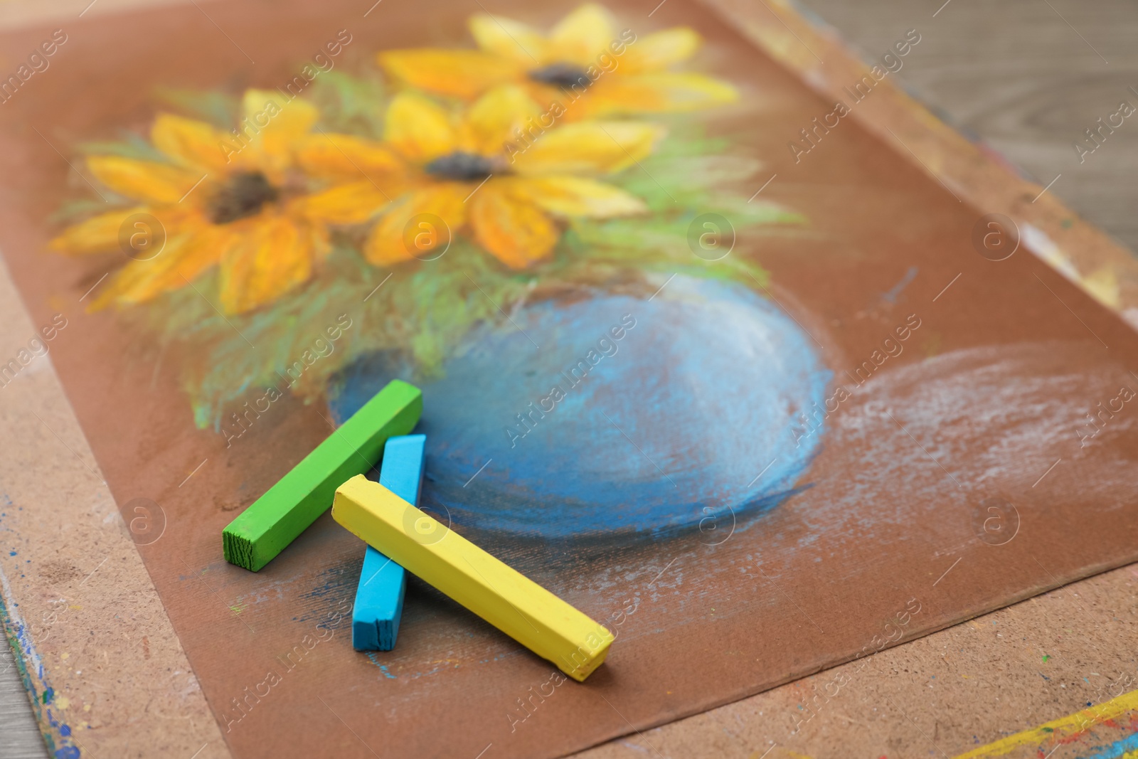 Photo of Beautiful drawing of yellow flowers and pastels on table, closeup