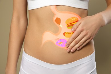 Image of Woman with image of stomach full of junk food drawn on her belly against beige background, closeup. Unhealthy eating habits